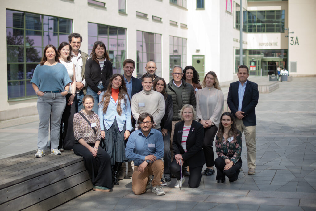 Group photo of 17 project partners taken during the kickoff meeting in Borås, Sweden, in May 2025. The group is posed outdoors in front of a modern white building with large windows.
