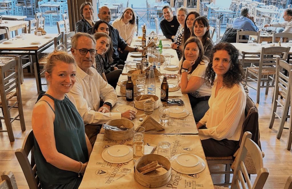 13 members sat at a long tavern table semi-outdoors at the beginning of a meal. 