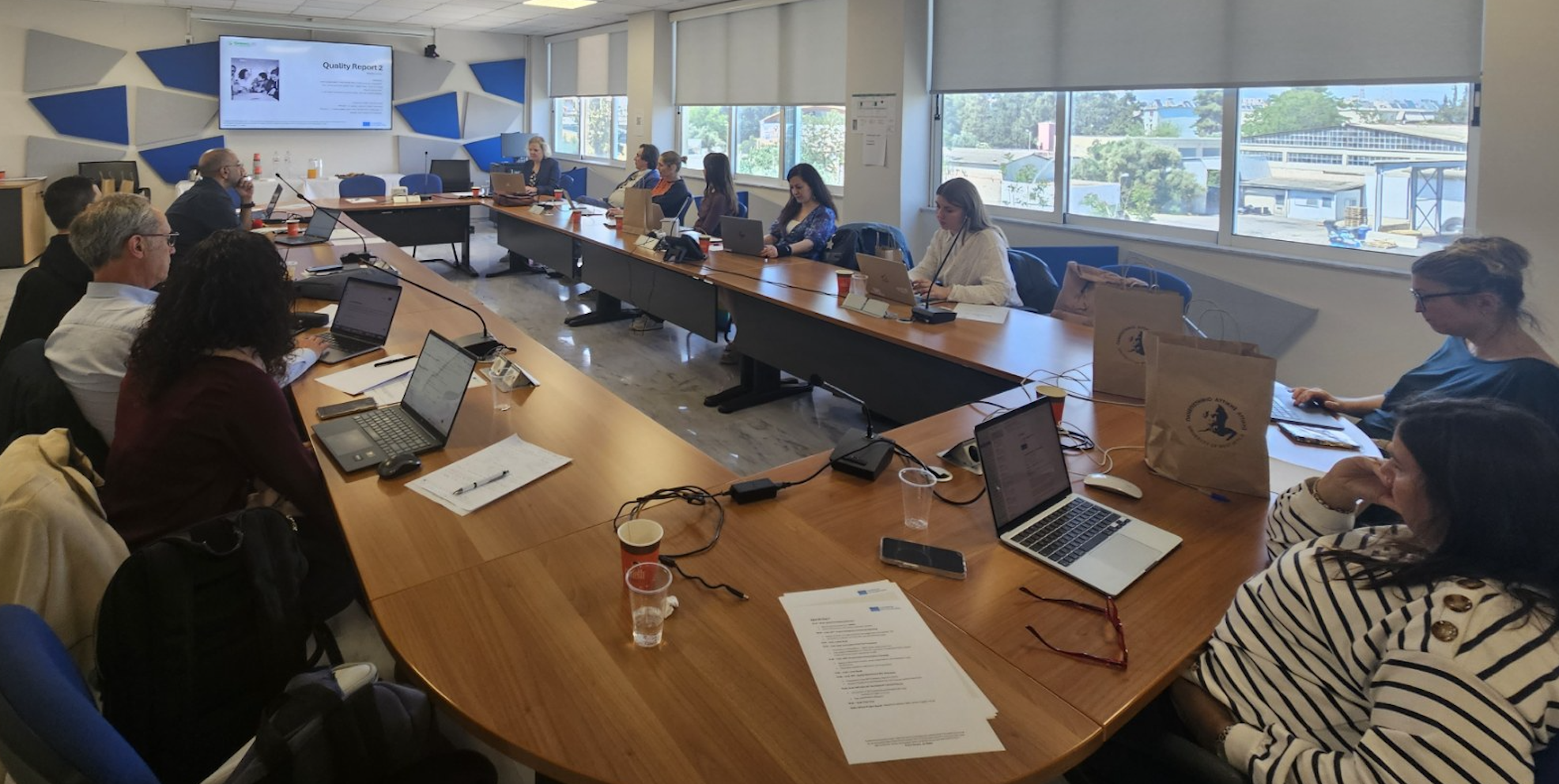 Hard at work. 13 people around a large conference table, some working on laptops, others looking at the PPT displayed on the screen.